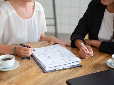 Young female colleagues meeting and discussing business plan, writing strategy scheme on paper, making draft. Cropped shot. Planning concept